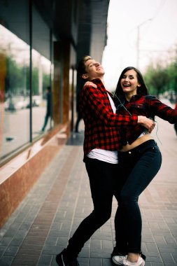 Kulaklık ile müzik dinlemek, birbirlerine söz ve gülümseyen yürüyüş ve şehirde dans iki mutlu trendy genç arkadaş. Yaşam tarzı, dostluk ve kentsel yaşam kavramları.