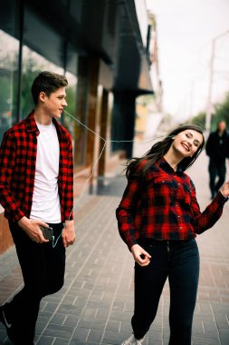 Kulaklık ile müzik dinlemek, birbirlerine söz ve gülümseyen yürüyüş ve şehirde dans iki mutlu trendy genç arkadaş. Yaşam tarzı, dostluk ve kentsel yaşam kavramları.