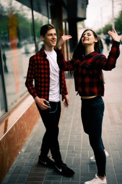 Kulaklık ile müzik dinlemek, birbirlerine söz ve gülümseyen yürüyüş ve şehirde dans iki mutlu trendy genç arkadaş. Yaşam tarzı, dostluk ve kentsel yaşam kavramları.