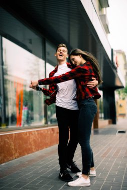 Kulaklık ile müzik dinlemek, birbirlerine söz ve gülümseyen yürüyüş ve şehirde dans iki mutlu trendy genç arkadaş. Yaşam tarzı, dostluk ve kentsel yaşam kavramları.