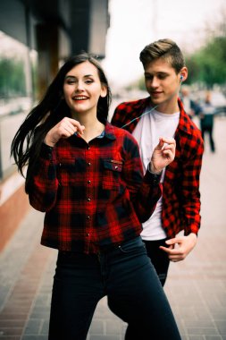 Kulaklık ile müzik dinlemek, birbirlerine söz ve gülümseyen yürüyüş ve şehirde dans iki mutlu trendy genç arkadaş. Yaşam tarzı, dostluk ve kentsel yaşam kavramları.