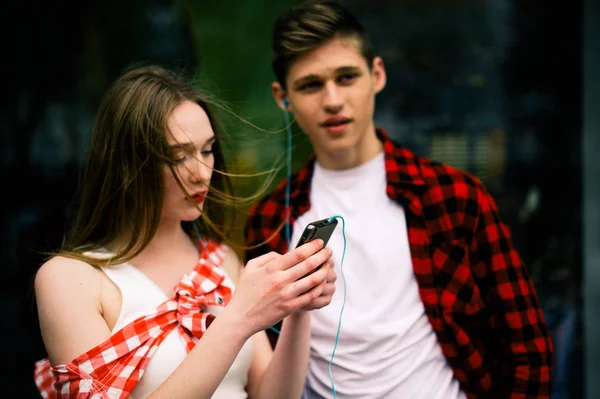 Två glada trendiga tonåriga vänner promenader och dans i staden, lyssna på musik med hörlurar, prata varandra och ler. Livsstil, vänskap och stadslivet begrepp. — Stockfoto