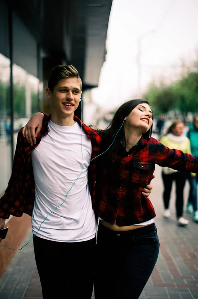 Zwei fröhliche trendige Teenager-Freunde, die durch die Stadt spazieren und tanzen, die Musik mit Kopfhörern hören, miteinander reden und lächeln. Lebensstil, Freundschaft und urbane Lebenskonzepte. — Stockfoto