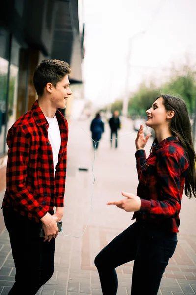 Due allegri amici adolescenti alla moda che passeggiano e ballano in città, ascoltano la musica con le cuffie, si parlano e sorridono. Stile di vita, amicizia e concetti di vita urbana . — Foto Stock