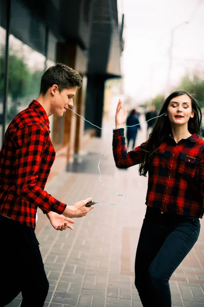 Dos felices amigos adolescentes de moda caminando y bailando en la ciudad, escuchando la música con auriculares, hablando entre sí y sonriendo. Conceptos de estilo de vida, amistad y vida urbana . —  Fotos de Stock