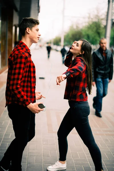 Zwei fröhliche trendige Teenager-Freunde, die durch die Stadt spazieren und tanzen, die Musik mit Kopfhörern hören, miteinander reden und lächeln. Lebensstil, Freundschaft und urbane Lebenskonzepte. — Stockfoto