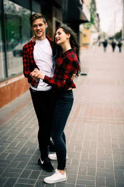 Dois felizes amigos adolescentes da moda andando e dançando na cidade, ouvindo a música com fones de ouvido, conversando uns com os outros e sorrindo. Estilo de vida, amizade e conceitos de vida urbana . — Fotografia de Stock