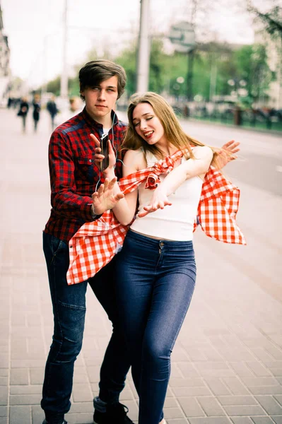Två glada trendiga tonåriga vänner promenader och dans i staden, lyssna på musik med hörlurar, prata varandra och ler. Livsstil, vänskap och stadslivet begrepp. — Stockfoto