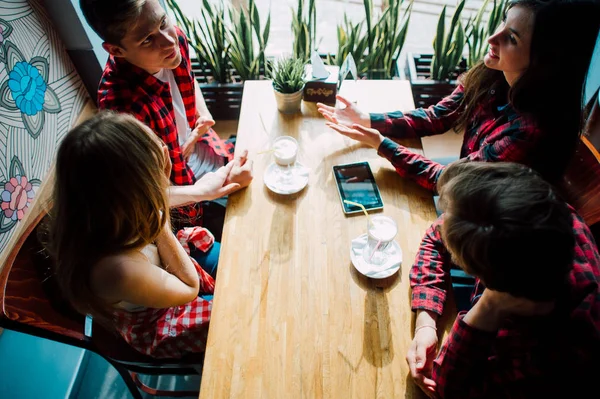 Un grupo de jóvenes amigos pasando el rato en una cafetería. Hombres y mujeres jóvenes que se reúnen en un café divirtiéndose y tomando café. Conceptos de estilo de vida, amistad y vida urbana . — Foto de Stock