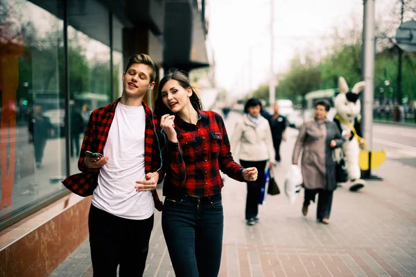 Dos felices amigos adolescentes de moda caminando y bailando en la ciudad, escuchando la música con auriculares, hablando entre sí y sonriendo. Conceptos de estilo de vida, amistad y vida urbana . — Foto de Stock