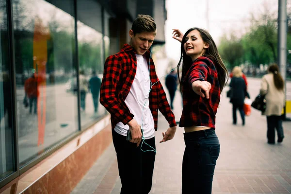 Zwei fröhliche trendige Teenager-Freunde, die durch die Stadt spazieren und tanzen, die Musik mit Kopfhörern hören, miteinander reden und lächeln. Lebensstil, Freundschaft und urbane Lebenskonzepte. — Stockfoto