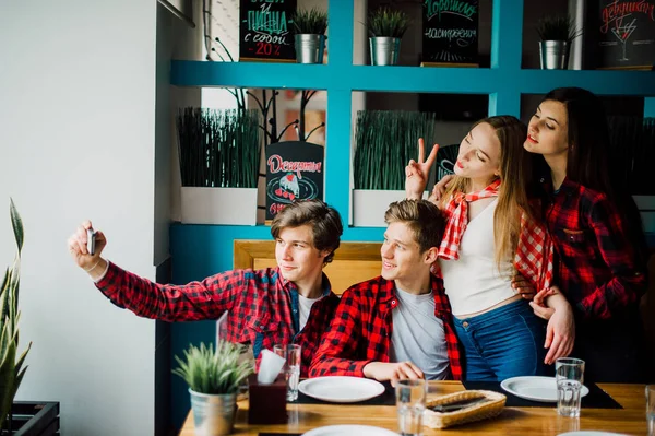 Un grupo de jóvenes amigos pasando el rato en una cafetería. Hombres y mujeres jóvenes que se reúnen en un café divirtiéndose y tomando café. Conceptos de estilo de vida, amistad y vida urbana . — Foto de Stock