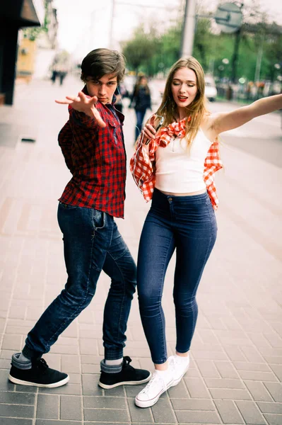Dois felizes amigos adolescentes da moda andando e dançando na cidade, ouvindo a música com fones de ouvido, conversando uns com os outros e sorrindo. Estilo de vida, amizade e conceitos de vida urbana . — Fotografia de Stock