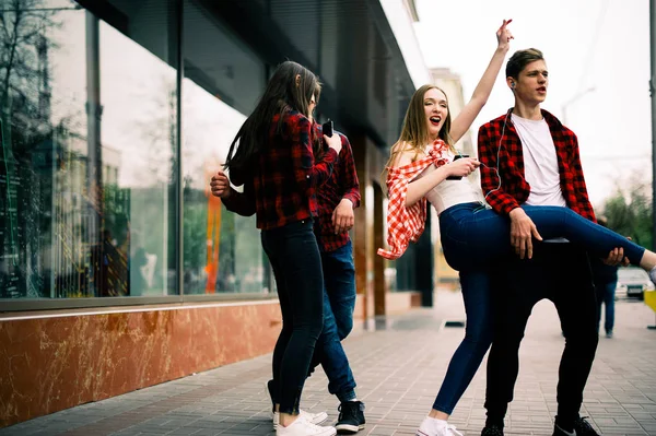 Deux amis adolescents joyeux et branchés marchent et dansent en ville, écoutent la musique avec des écouteurs, se parlent et sourient. Style de vie, amitié et concepts de vie urbaine . — Photo