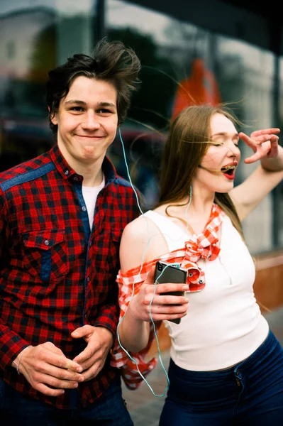 Dos felices amigos adolescentes de moda caminando y bailando en la ciudad, escuchando la música con auriculares, hablando entre sí y sonriendo. Conceptos de estilo de vida, amistad y vida urbana . — Foto de Stock