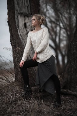 güzel sarışın genç kadın bahar arka plan, orman, göl, ağaçlar üzerinde beyaz kazak uzun etekle mavi gözlü. Soğuk ruh hali. Moda, duygusal portre