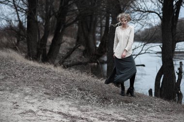 güzel sarışın genç kadın bahar arka plan, orman, göl, ağaçlar üzerinde beyaz kazak uzun etekle mavi gözlü. Soğuk ruh hali. Moda, duygusal portre