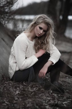 güzel sarışın genç kadın bahar arka plan, orman, göl, ağaçlar üzerinde beyaz kazak uzun etekle mavi gözlü. Soğuk ruh hali. Moda, duygusal portre