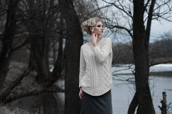 Bella giovane donna bionda con gli occhi azzurri in pullover bianco gonna lunga su sfondo primavera, foresta, lago, alberi. Freddo umore. Moda, ritratto emotivo — Foto Stock