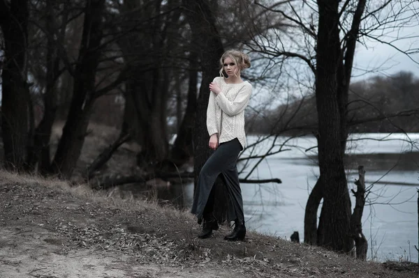 Mooie jonge blonde vrouw met blauwe ogen in de witte trui lange rok op voorjaar achtergrond, bomen, bos, lake. Koude sfeer. Mode, emotionele portret — Stockfoto