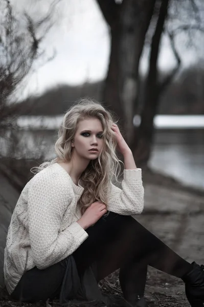 Hermosa mujer rubia joven con ojos azules en falda larga jersey blanco sobre fondo de primavera, bosque, lago, árboles. Humor frío. Moda, retrato emocional — Foto de Stock