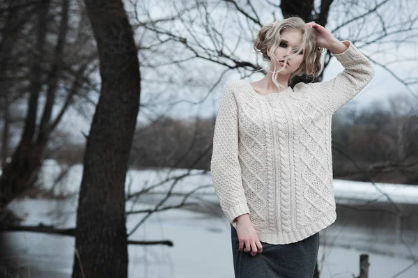 Bella giovane donna bionda con gli occhi azzurri in pullover bianco gonna lunga su sfondo primavera, foresta, lago, alberi. Freddo umore. Moda, ritratto emotivo — Foto Stock