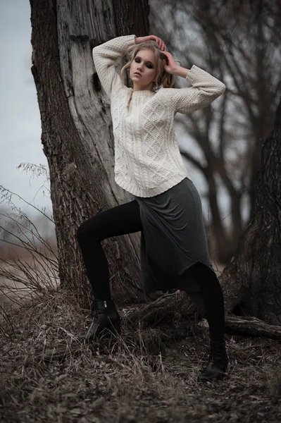 güzel sarışın genç kadın bahar arka plan, orman, göl, ağaçlar üzerinde beyaz kazak uzun etekle mavi gözlü. Soğuk ruh hali. Moda, duygusal portre