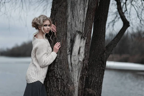 Mooie jonge blonde vrouw met blauwe ogen in de witte trui lange rok op voorjaar achtergrond, bomen, bos, lake. Koude sfeer. Mode, emotionele portret — Stockfoto