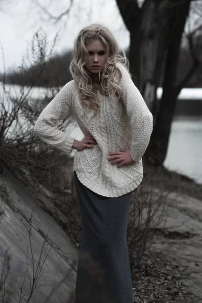 Mooie jonge blonde vrouw met blauwe ogen in de witte trui lange rok op voorjaar achtergrond, bomen, bos, lake. Koude sfeer. Mode, emotionele portret — Stockfoto