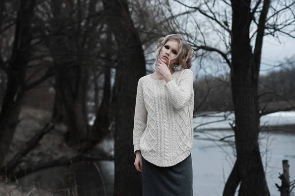 Mooie jonge blonde vrouw met blauwe ogen in de witte trui lange rok op voorjaar achtergrond, bomen, bos, lake. Koude sfeer. Mode, emotionele portret — Stockfoto