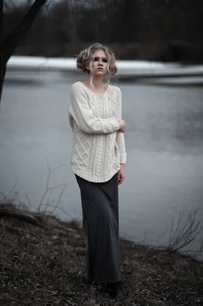 Bela jovem mulher loira com olhos azuis em pulôver branco saia longa no fundo da primavera, floresta, lago, árvores. Humor frio. Moda, retrato emocional — Fotografia de Stock