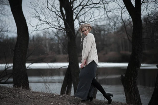 Mooie jonge blonde vrouw met blauwe ogen in de witte trui lange rok op voorjaar achtergrond, bomen, bos, lake. Koude sfeer. Mode, emotionele portret — Stockfoto