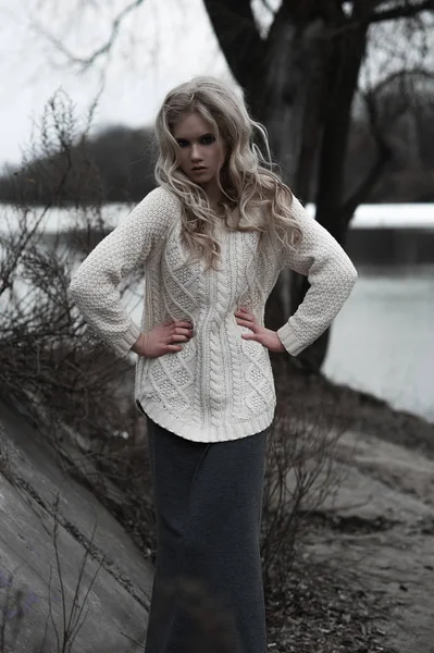 Bela jovem mulher loira com olhos azuis em pulôver branco saia longa no fundo da primavera, floresta, lago, árvores. Humor frio. Moda, retrato emocional — Fotografia de Stock