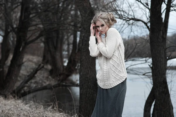 Bela jovem mulher loira com olhos azuis em pulôver branco saia longa no fundo da primavera, floresta, lago, árvores. Humor frio. Moda, retrato emocional — Fotografia de Stock