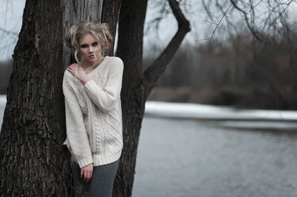 Mooie jonge blonde vrouw met blauwe ogen in de witte trui lange rok op voorjaar achtergrond, bomen, bos, lake. Koude sfeer. Mode, emotionele portret — Stockfoto