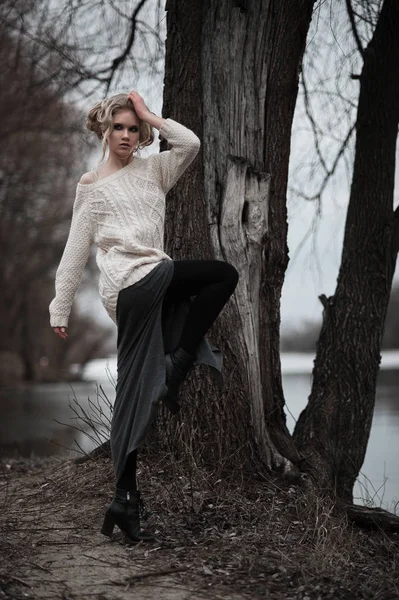 Mooie jonge blonde vrouw met blauwe ogen in de witte trui lange rok op voorjaar achtergrond, bomen, bos, lake. Koude sfeer. Mode, emotionele portret — Stockfoto