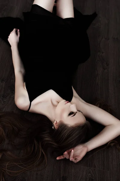 Fiatal lány, szép hosszú haja és füstös szemek rajta fekete maxi estélyi ruhában pózol egy tükör. Stúdió felvétel — Stock Fotó