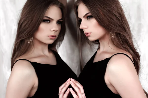 Молодая девушка с длинными красивыми волосами и дымчатыми глазами в черном макси вечернее платье позирует с зеркалом. Снимок студии — стоковое фото