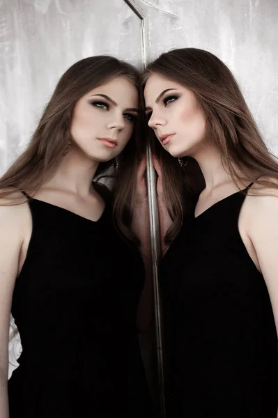 Mladá dívka s dlouhé krásné vlasy a kouřové oči nosí černé maxi večerní šaty pózuje se zrcadlem. Studio záběr — Stock fotografie