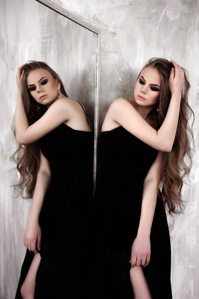 Menina com cabelos longos e bonitos e olhos fumegantes vestindo vestido de noite maxi preto posando com um espelho. Estúdio — Fotografia de Stock