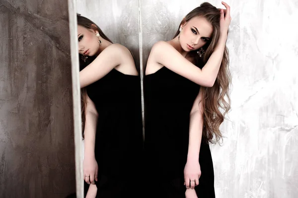 Jong meisje met lange mooie haren en rokerige ogen dragen zwarte maxi avondjurk poseren met een spiegel. Studio schoot — Stockfoto