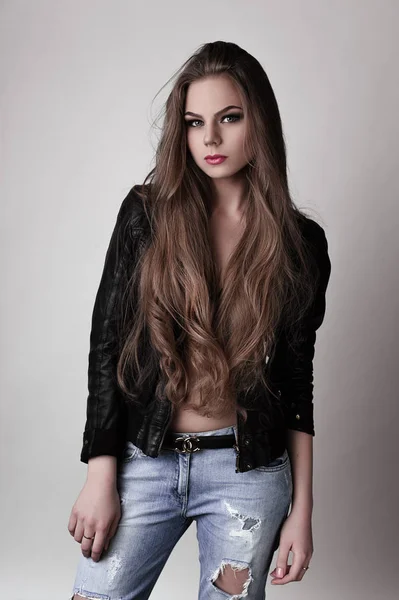 Jeune fille aux longs beaux cheveux et aux yeux fumés portant une veste et un jean en cuir noir. Plan studio . — Photo