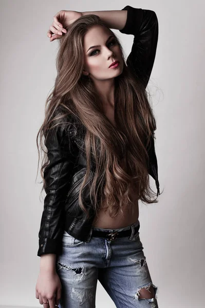 Jeune fille aux longs beaux cheveux et aux yeux fumés portant une veste et un jean en cuir noir. Plan studio . — Photo