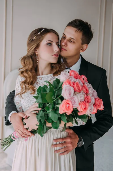Niedliche Hochzeitspaar im Inneren eines klassischen weißen Studio dekoriert. hey küssen und umarmen einander, Händchen haltend, einander anschauend — Stockfoto