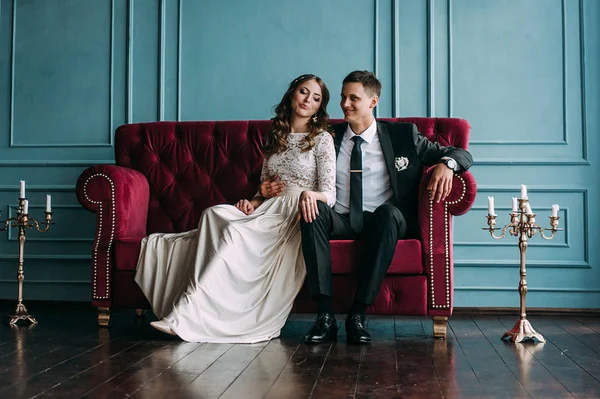 Cute wedding couple in the interior of a classic studio posing at the sofa . hey kiss and hug each other, holding hands looking at each other — Stock Photo, Image