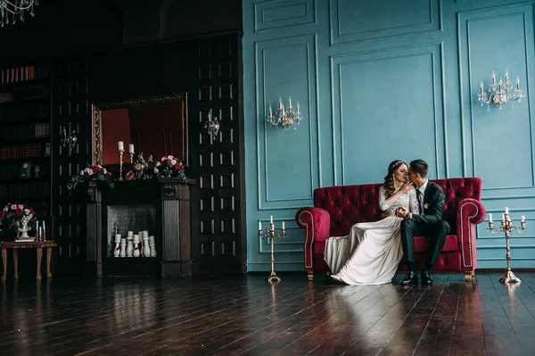 Schattig bruidspaar in het interieur van een klassieke studio poseren op de Bank. Hey kussen en omhelzen elkaar, hand in hand kijken naar elkaar — Stockfoto