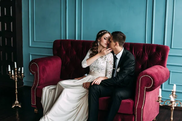 Cute wedding couple in the interior of a classic studio posing at the sofa . hey kiss and hug each other, holding hands looking at each other — Stock Photo, Image