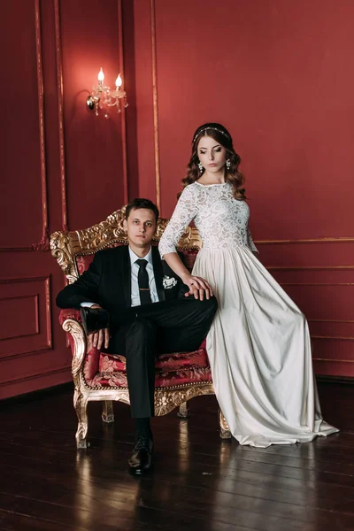 Cute wedding couple in the interior of a classic studio with red background . hey kiss and hug each other, holding hands looking at each other — Stock Photo, Image