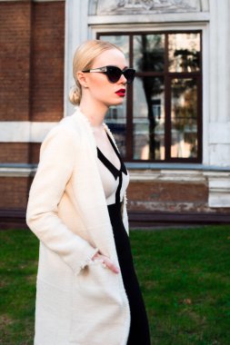 Mutlu moda sarışın Avrupa zarif kadın kırmızı dudakları ve beyaz ayakta yeşil çimenlerin üzerinde bina eski kırmızı tuğla, Cilt. Seksi kız açık havada. Resmi siyah beyaz elbiseli güzel kadın 