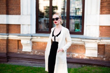 Mutlu moda sarışın Avrupa zarif kadın kırmızı dudakları ve beyaz ayakta yeşil çimenlerin üzerinde bina eski kırmızı tuğla, Cilt. Seksi kız açık havada. Resmi siyah beyaz elbiseli güzel kadın 